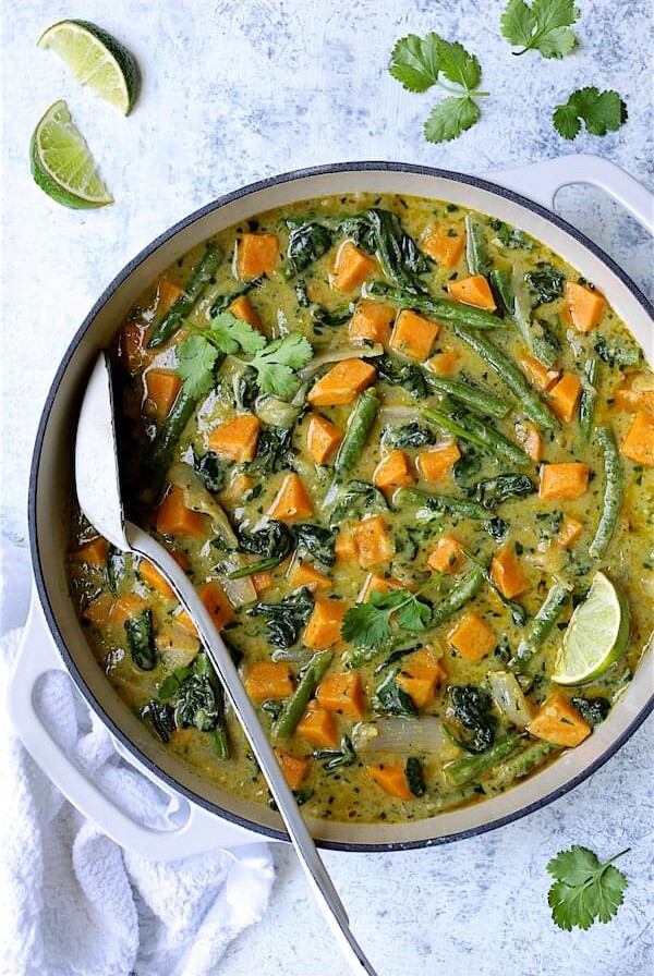 Vegan Thai Green Sweet Potato Curry in white enamel cast iron skillet garnished with cilantro and lime wedges.