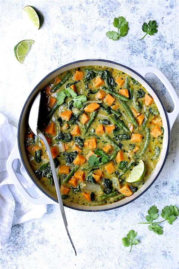 Photo of Vegan Thai Green Sweet Potato Curry on pale blue background garnished with cilantro and lime wedges.