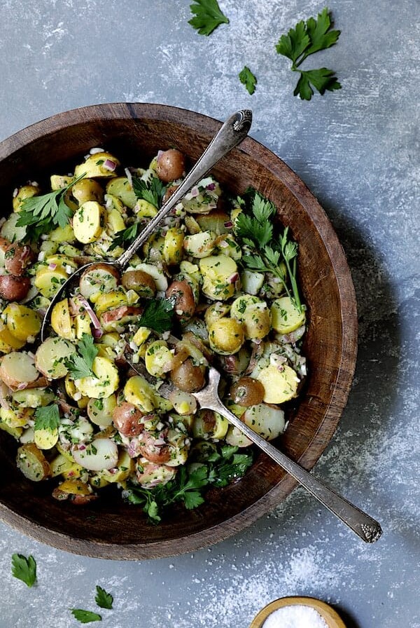 French-Style Potato Salad in wooden bowl with serving utensils garnished with fresh parsley.