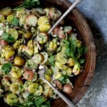 French-Style Potato Salad in wooden bowl with serving utensils garnished with fresh parsley.