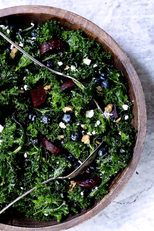 Photo of Massaged Kale, Beet and Blueberry Salad with Honey - Balsamic Dressing being tossed with serving utensils.