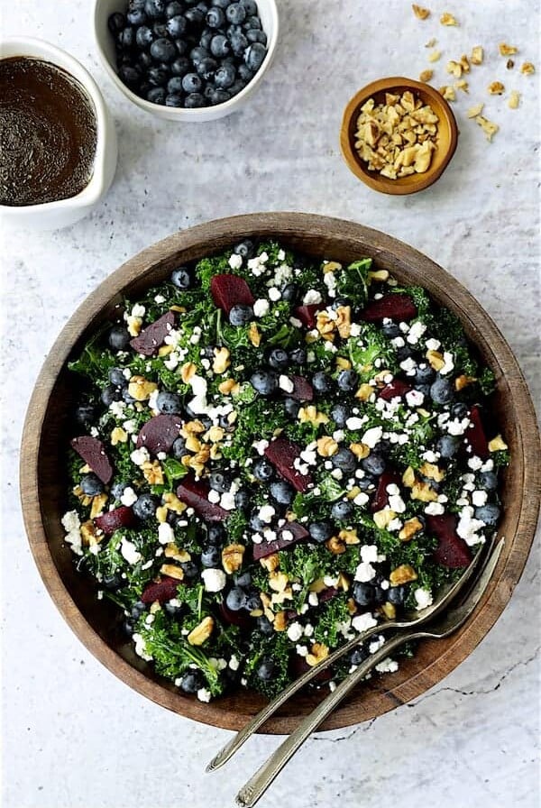 Massaged Kale, Beet and Blueberry Salad with Honey - Balsamic Dressing - Overhead hero shot of salad in wood bowl on gray stone background