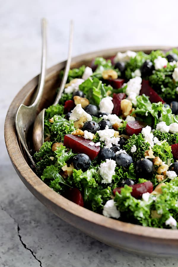 Close-up photo of Massaged Kale, Beet and Blueberry Salad with Honey - Balsamic Dressing assembled in wood bowl.