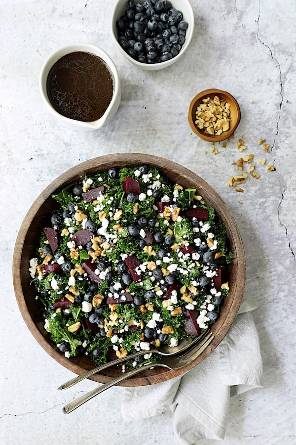 Photo of Massaged Kale, Beet and Blueberry Salad with Honey - Balsamic Dressing with dressing, blueberries and walnuts in small bowls on stone background.