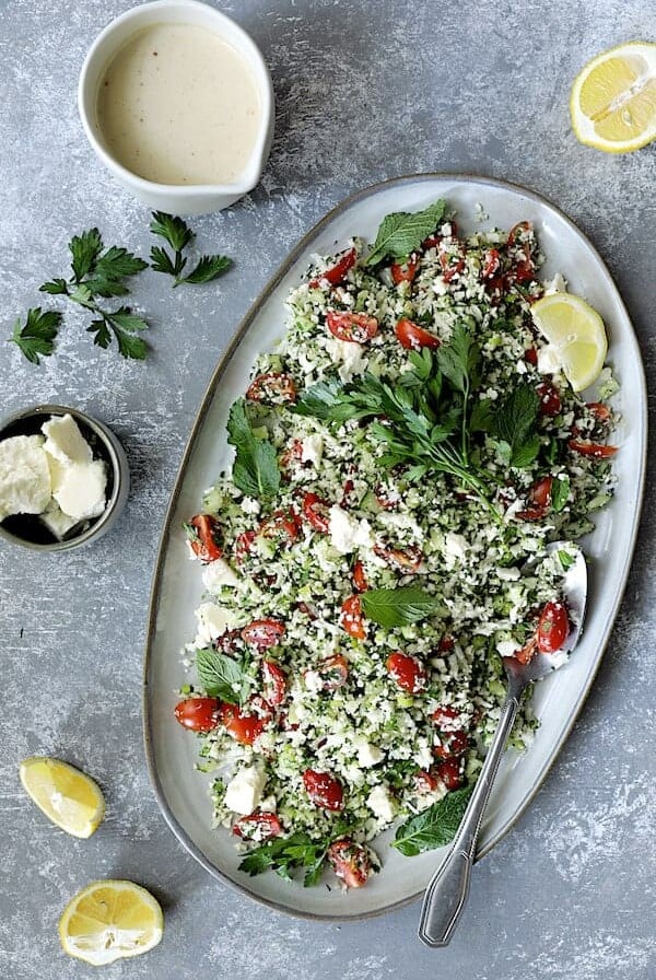 Cauliflower Tabouli with Lemon Tahini Dressing and Feta Cheese - Overhead hero shot of salad on large oval platter garnished with parsley and lemons