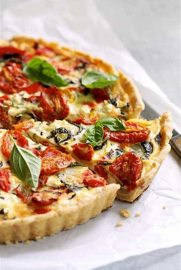 Provencal Vegetable and Goat Cheese Tart - Hero shot of tart on white parchment paper with a slice removed