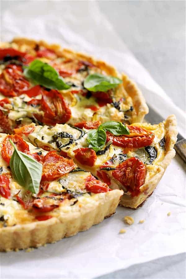 Photo of Provencal Vegetable and Goat Cheese Tart on white parchment paper with a slice cut from it.