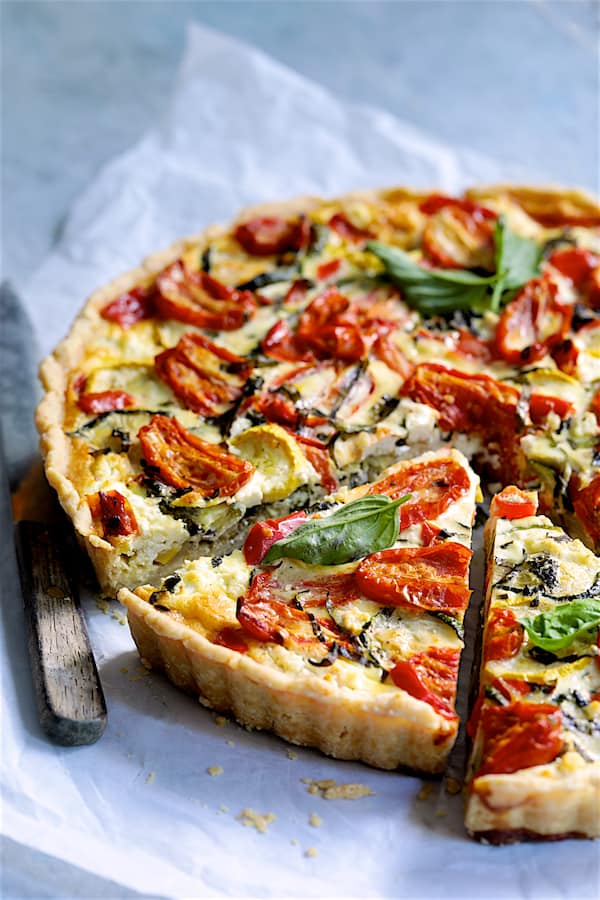 Photo of Provencal Vegetable and Goat Cheese Tart with tart slices on white parchment paper with knife.