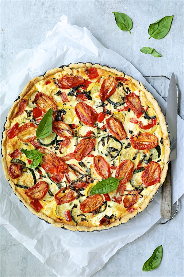 Photo of baked Provencal Vegetable and Goat Cheese Tart on parchment paper garnished with fresh basil.