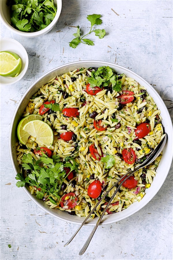 Photo of Southwestern Orzo Salad with Cilantro Lime Dressing - Overhead shot in white serving bowl garnished with lime wedges and cilantro.