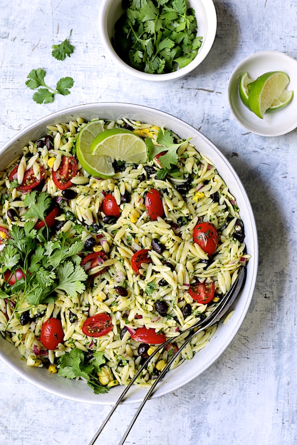 Photo of Southwestern Orzo Salad with Cilantro Lime Dressing in white serving bowl garnished with cilantro and lime.
