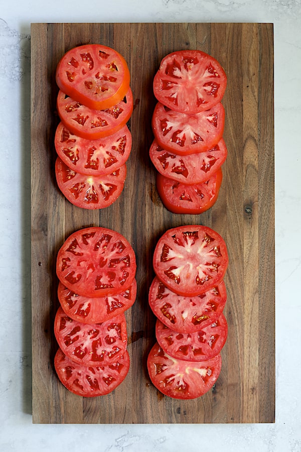 Photo of 16 tomato slices on wood cutting board.
