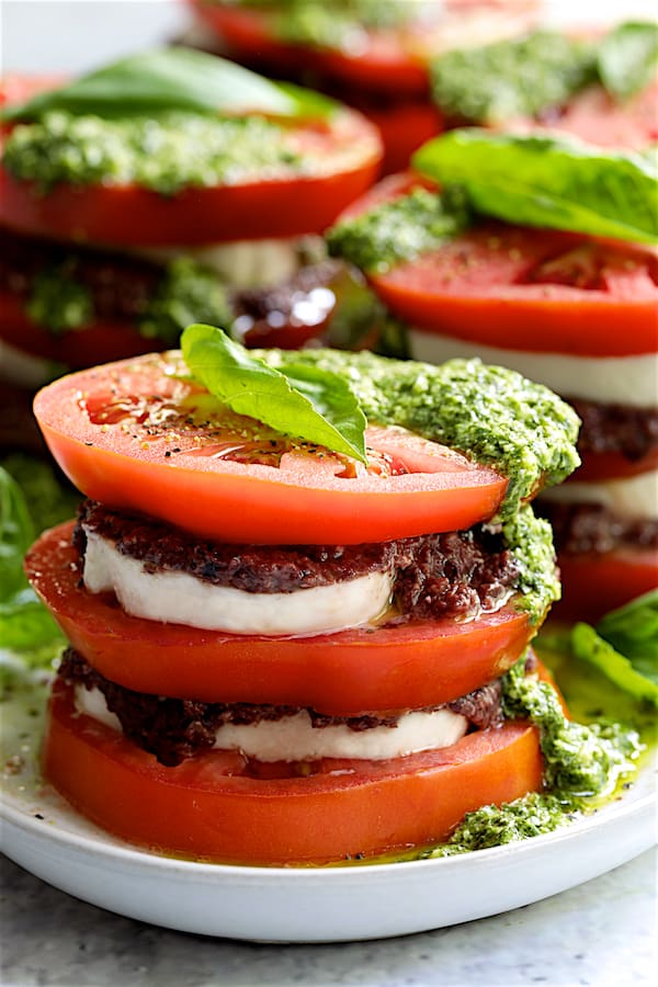 Close-up photo of Stacked Tomato Salad with Tapenade and Basil Pesto Dressing drizzled with dressing and garnished with fresh basil leaves.