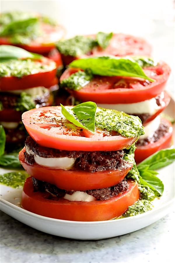 Photo of Stacked Tomato Salad with Tapenade and Basil Pesto Dressing on white platter.