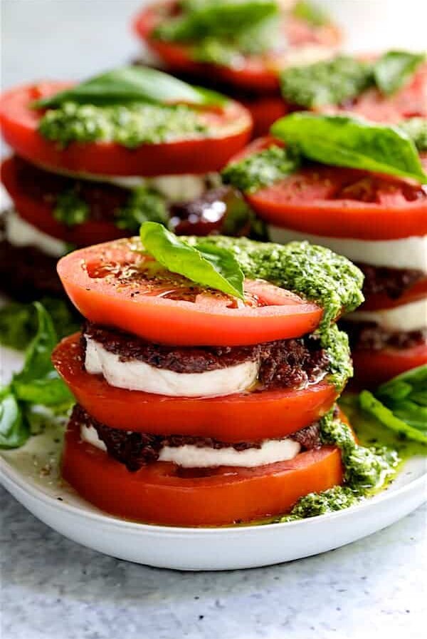 Stacked Tomato Salad with Tapenade and Basil Pesto Dressing - Close-up hero shot on white platter