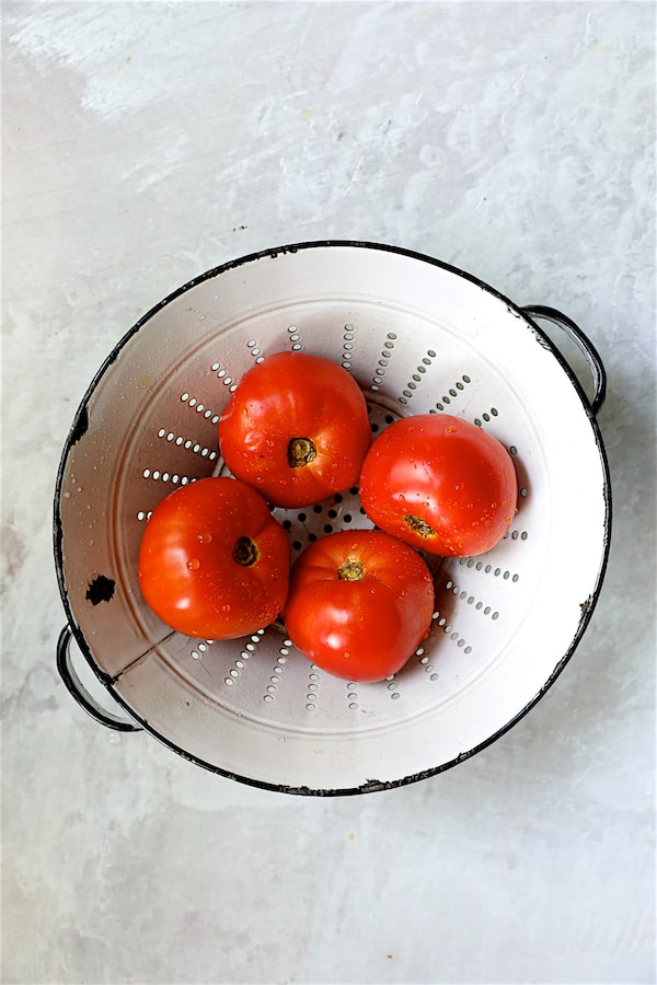 Photo of four tomatoes in white rustic colander.
