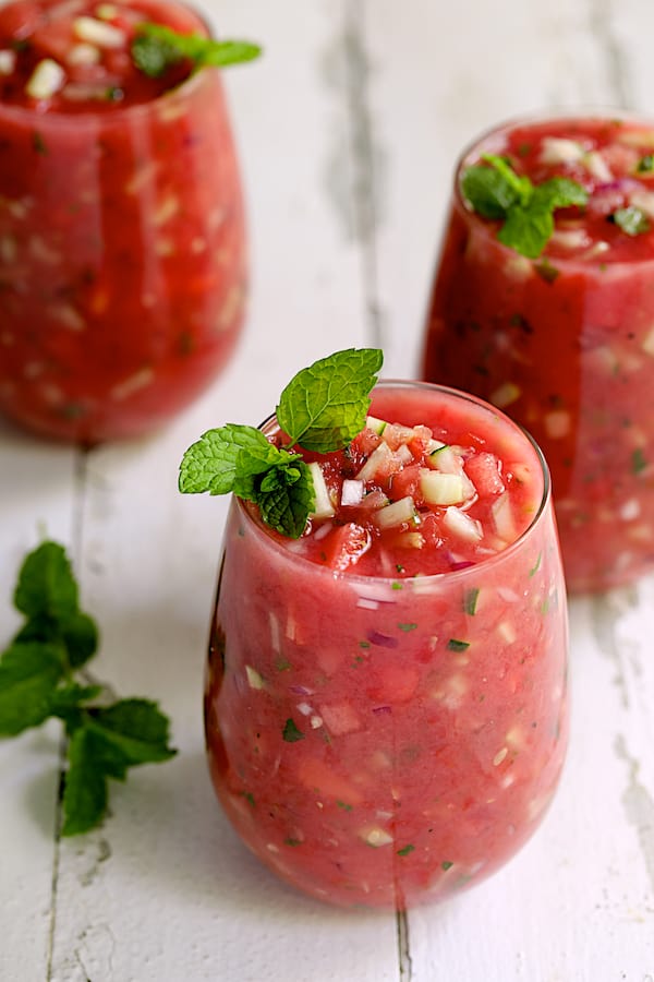 Photo of Watermelon Gazpacho with Serrano Chiles and Mint in three glasses of the soup on white distressed background.