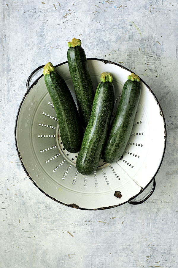 Photo of four zucchini in white distressed colander.
