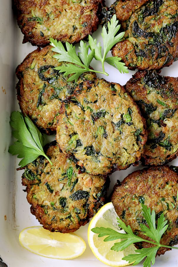 Close-up photo of Zucchini Red Lentil and Spinach Fritters with fresh greens and lemon wedges.