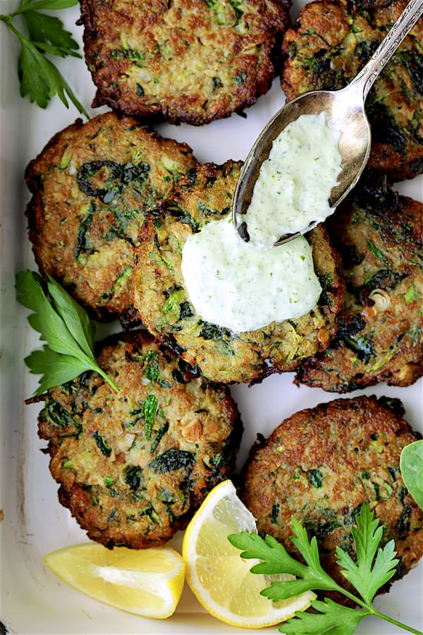 Photo of Zucchini Red Lentil and Spinach Fritters with Cilantro Yogurt Sauce with sauce being drizzled over fritters.