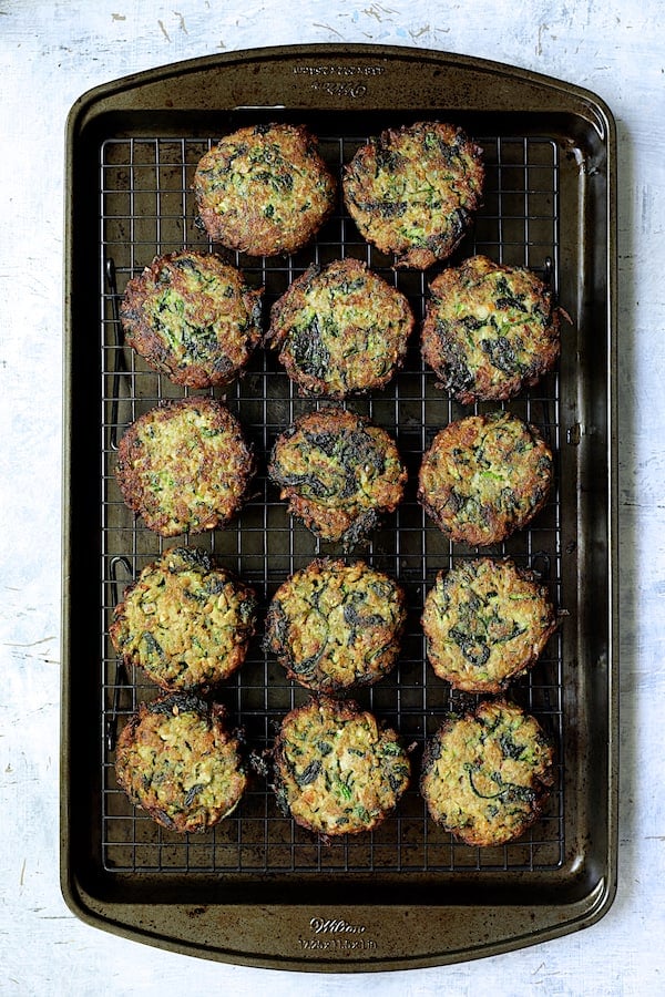 Photo of fried zucchini fritters on rack over baking sheet.