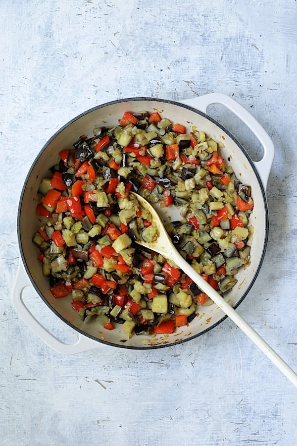 Photo of fresh ingredients for caponata being cooked in white cast iron skillet.