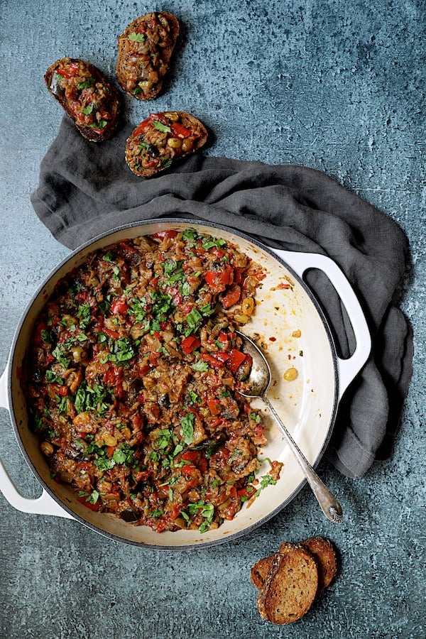 Photo of Moroccan-Spiced Caponata being served up on crusty bread from white cast iron skillet.