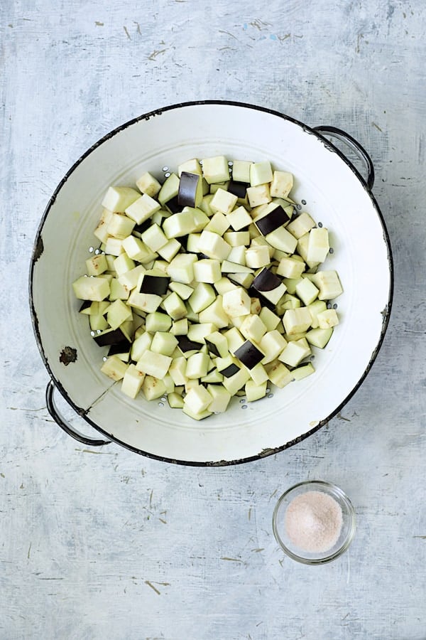 Photo of cubed eggplant in white distressed colander with salt.