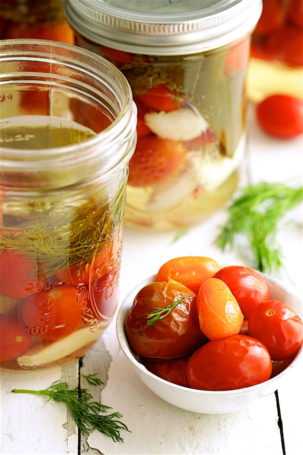 Close up photo of opened jar of Pickled Grape Tomatoes and some in small white bowl.