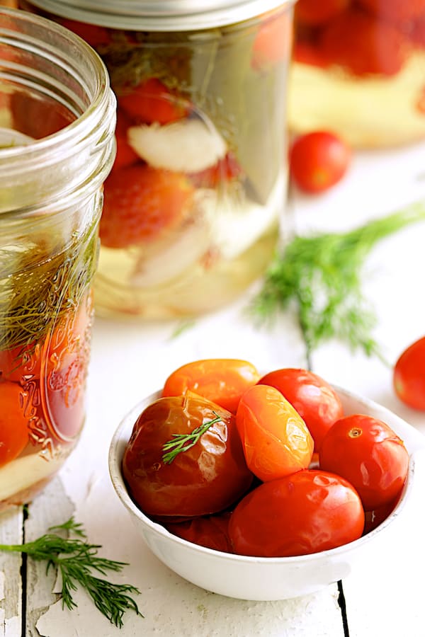 Close-up photo of pickled tomatoes in small white bowl garnished with dill/