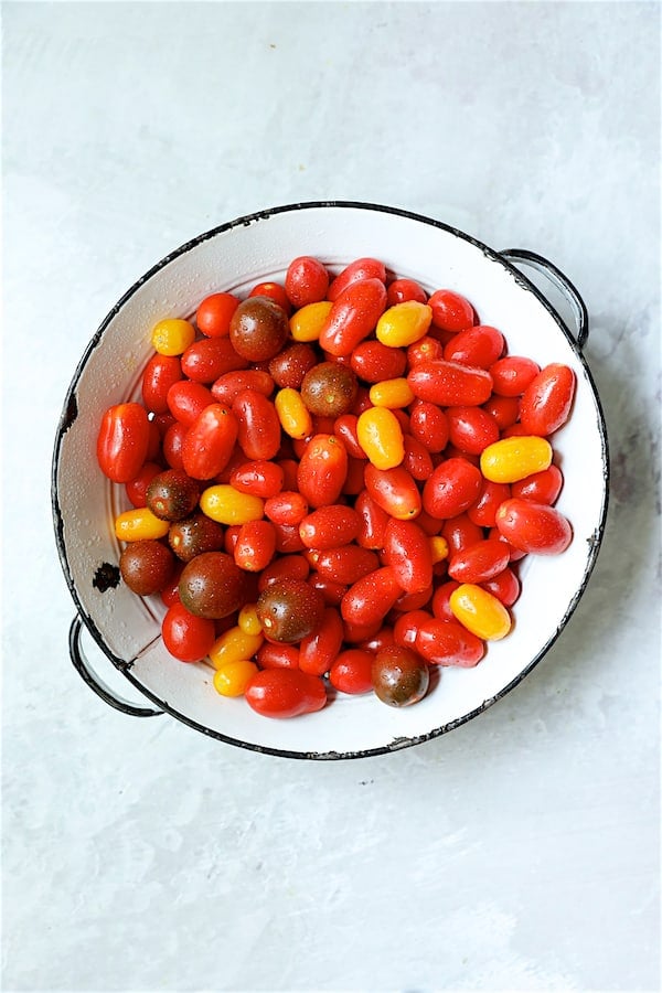 Photo of multicolored grape tomatoes in white antique colander on white background.