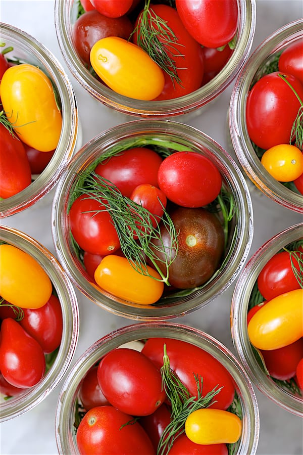 Top down close-up photo of tomatoes and other ingredients packed into glass pint jars.