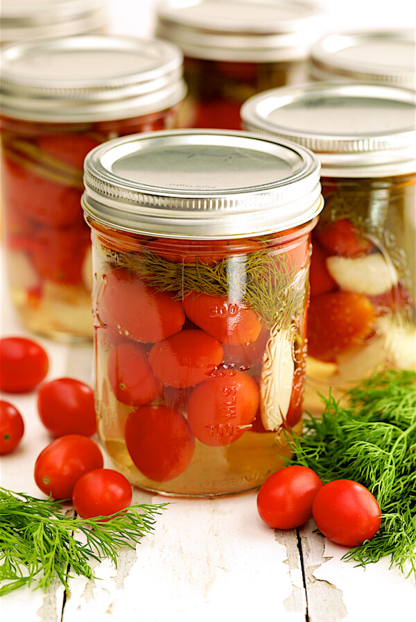Pickled Grape Tomatoes - Hero shot of tomatoes in glass pint jar with fresh tomatoes and dill scattered around.