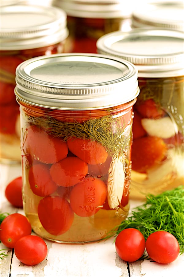 Photo of Pickled Grape Tomatoes in glass pint jar with fresh dill and tomatoes scattered about.