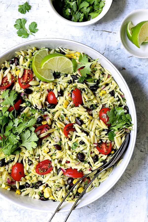 Photo of Southwestern Orzo Pasta Salad with Cilantro Lime Dressing in white serving bowl garnished with lime wedges and cilantro.