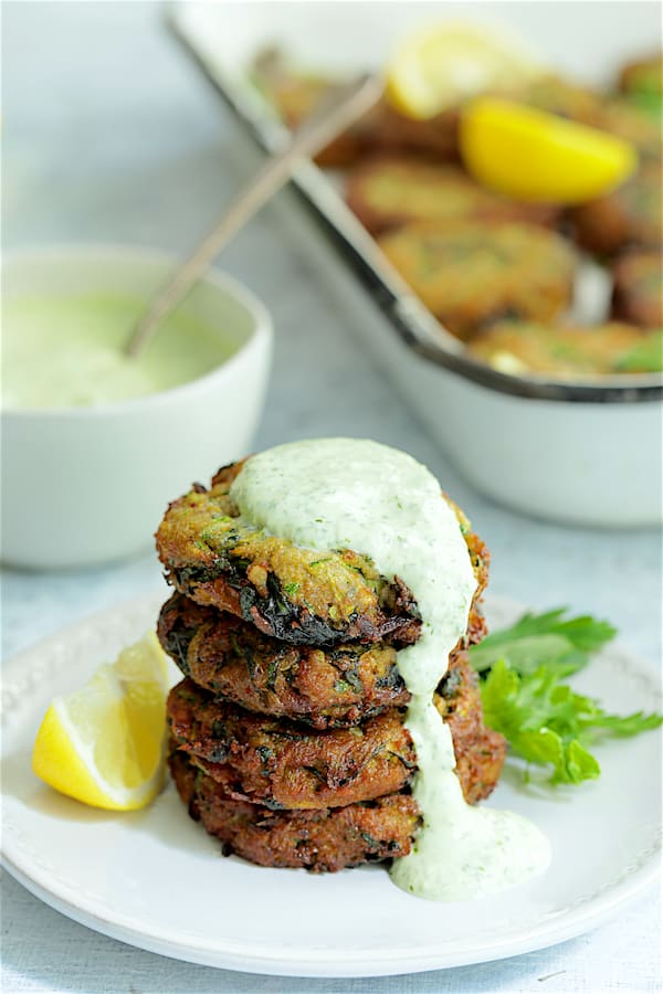 Photo of a stack of four Zucchini Red Lentil and Spinach Fritters with Cilantro Yogurt Sauce on white plate with sauce dripping down onto the plate.