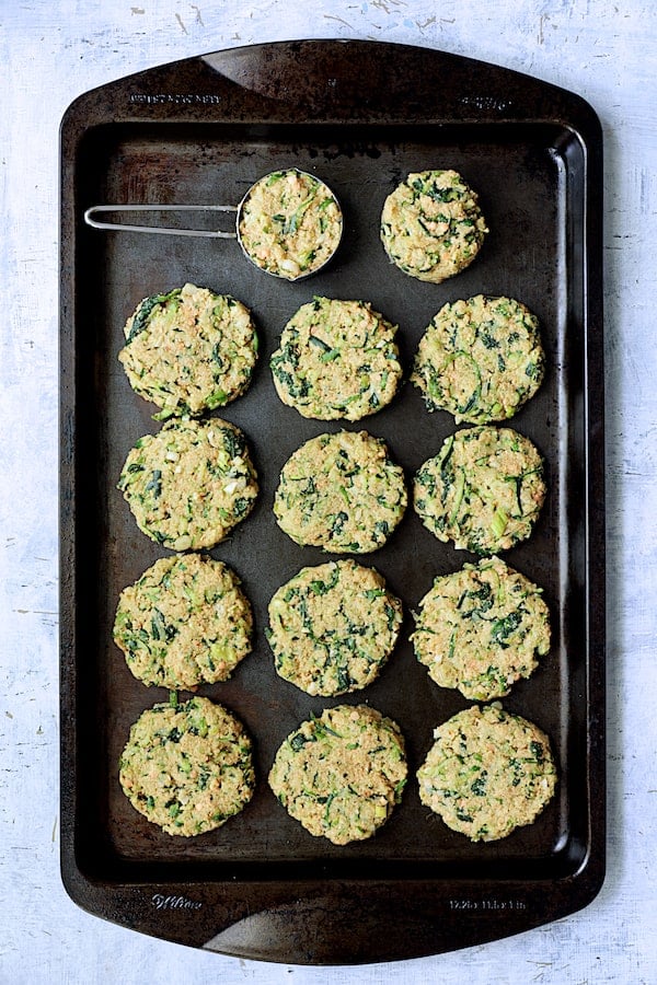 Photo of Zucchini, Red Lentil and Spinach Fritters on black baking sheet being being fried.
