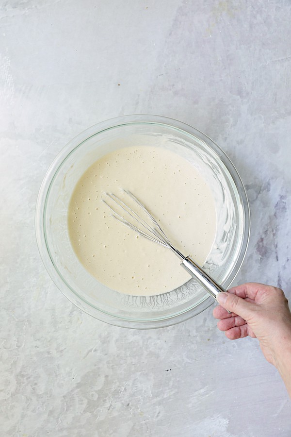 Photo of beer batter being stirred in glass bowl with wire whisk.