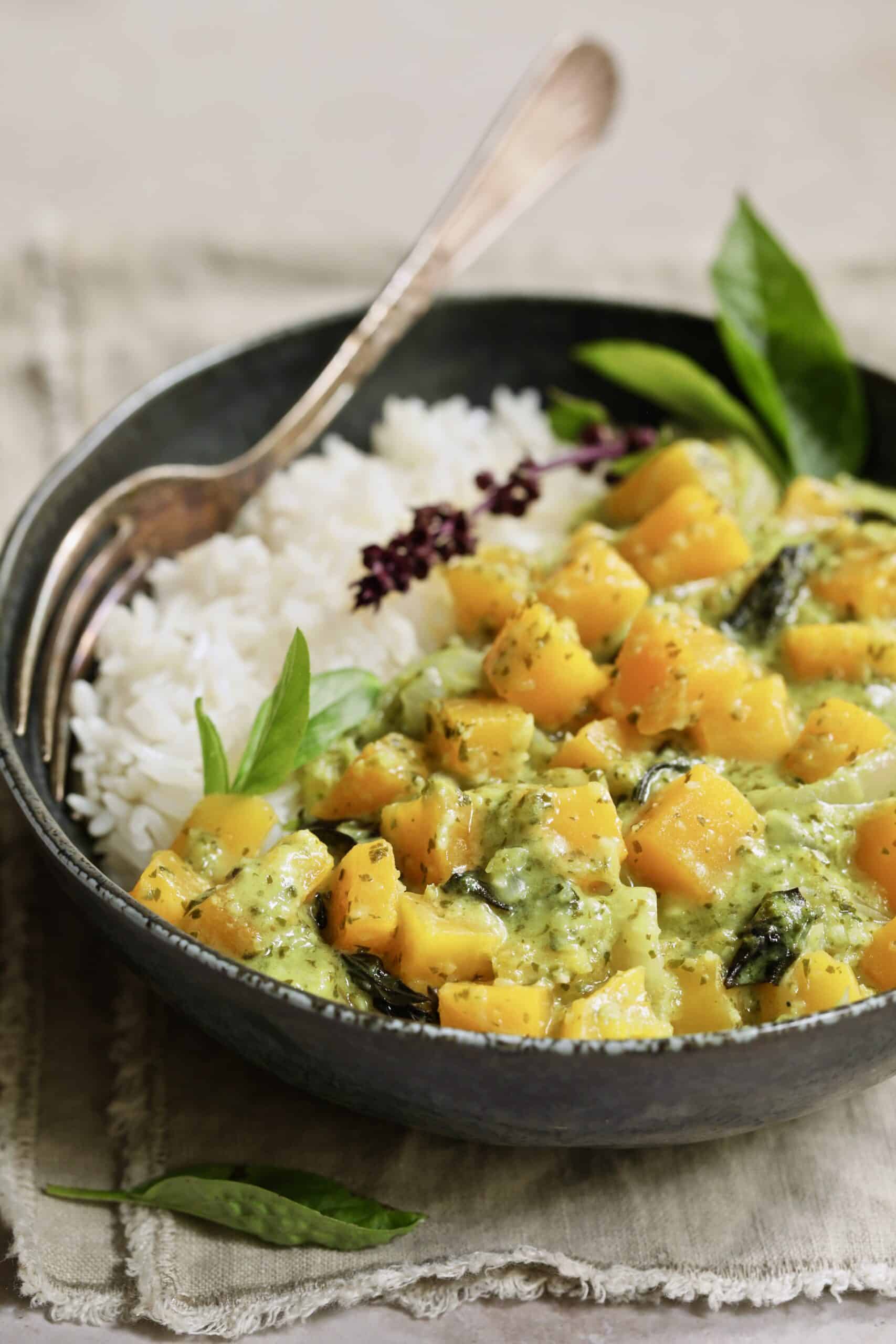 Close-up photo of Butternut Squash in Fresh Green Curry in black bowl garnished with Thai basil.
