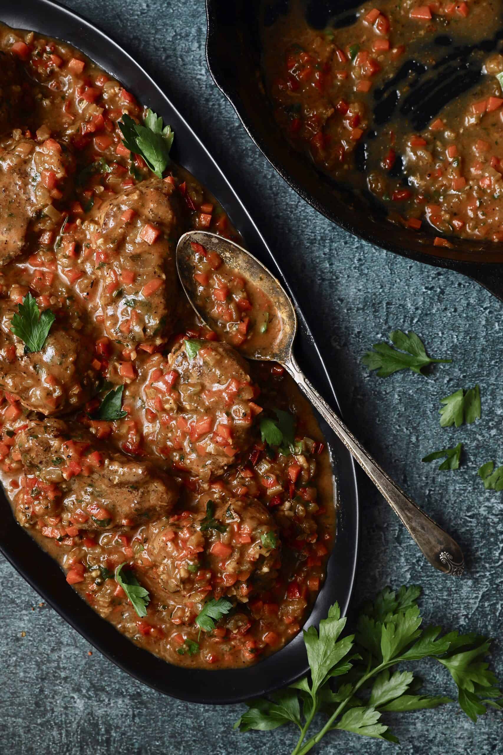 Photo of Cajun-Smothered Pork Medallions on black oval platter with serving spoon.