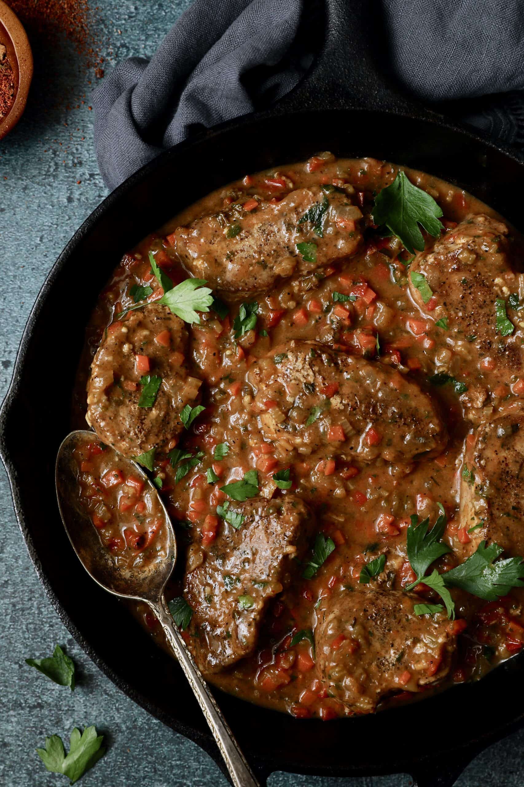 Close-up photo of Cajun-Smothered Pork Medallions in cast iron skillet with serving spoon.