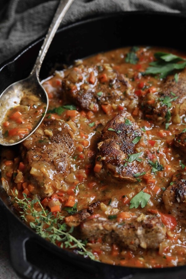 Cajun-Smothered Pork Medallions - Close-up shot in cast iron skillet with thyme sprigs