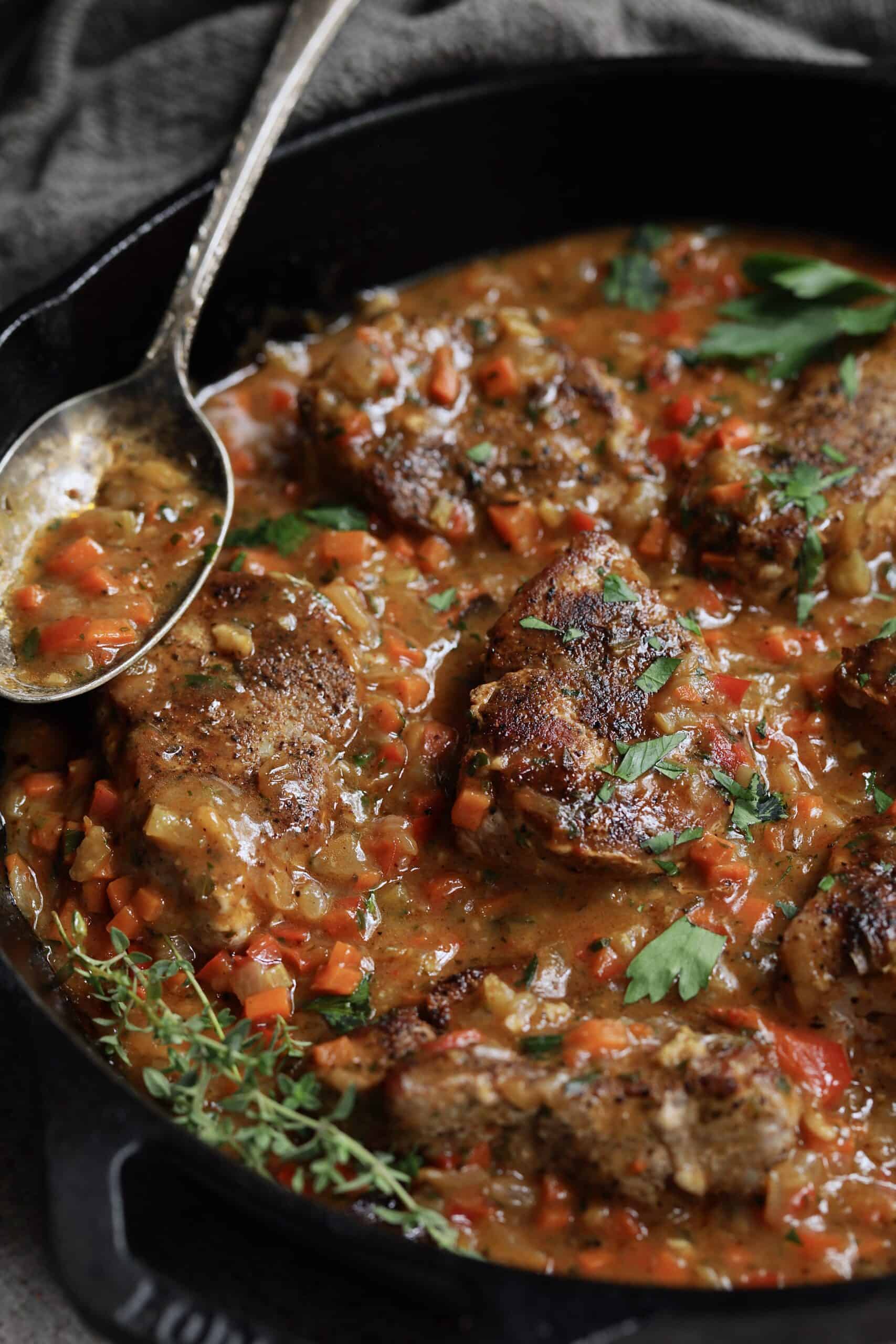 Photo of Cajun-Smothered Pork Medallions in cast iron skillet garnished with thyme sprigs.