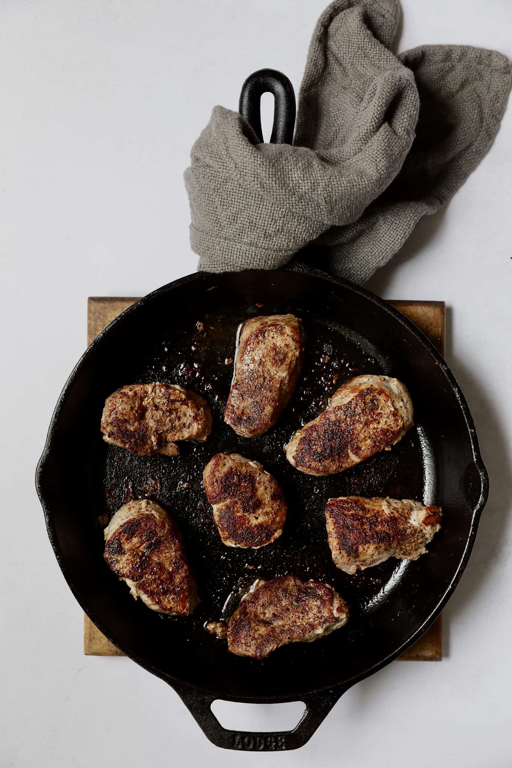 Photo of seared pork medallions in cast iron skillet.