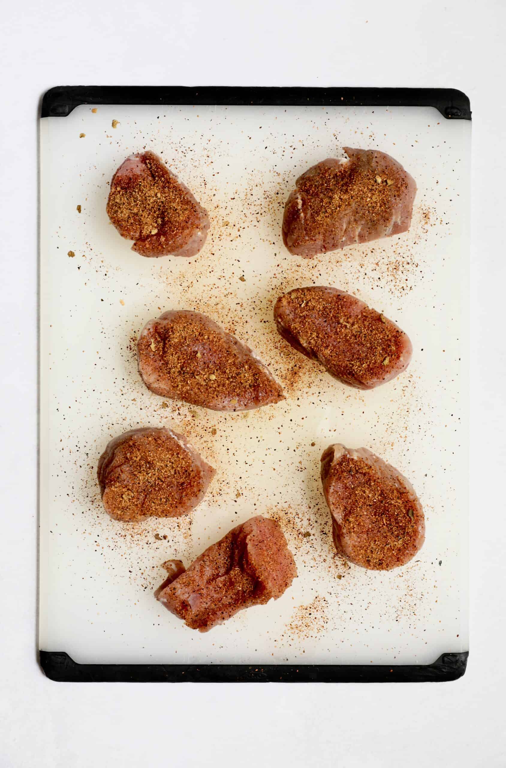 Photo of pork medallions sprinkled with Cajun seasoning on white cutting board.