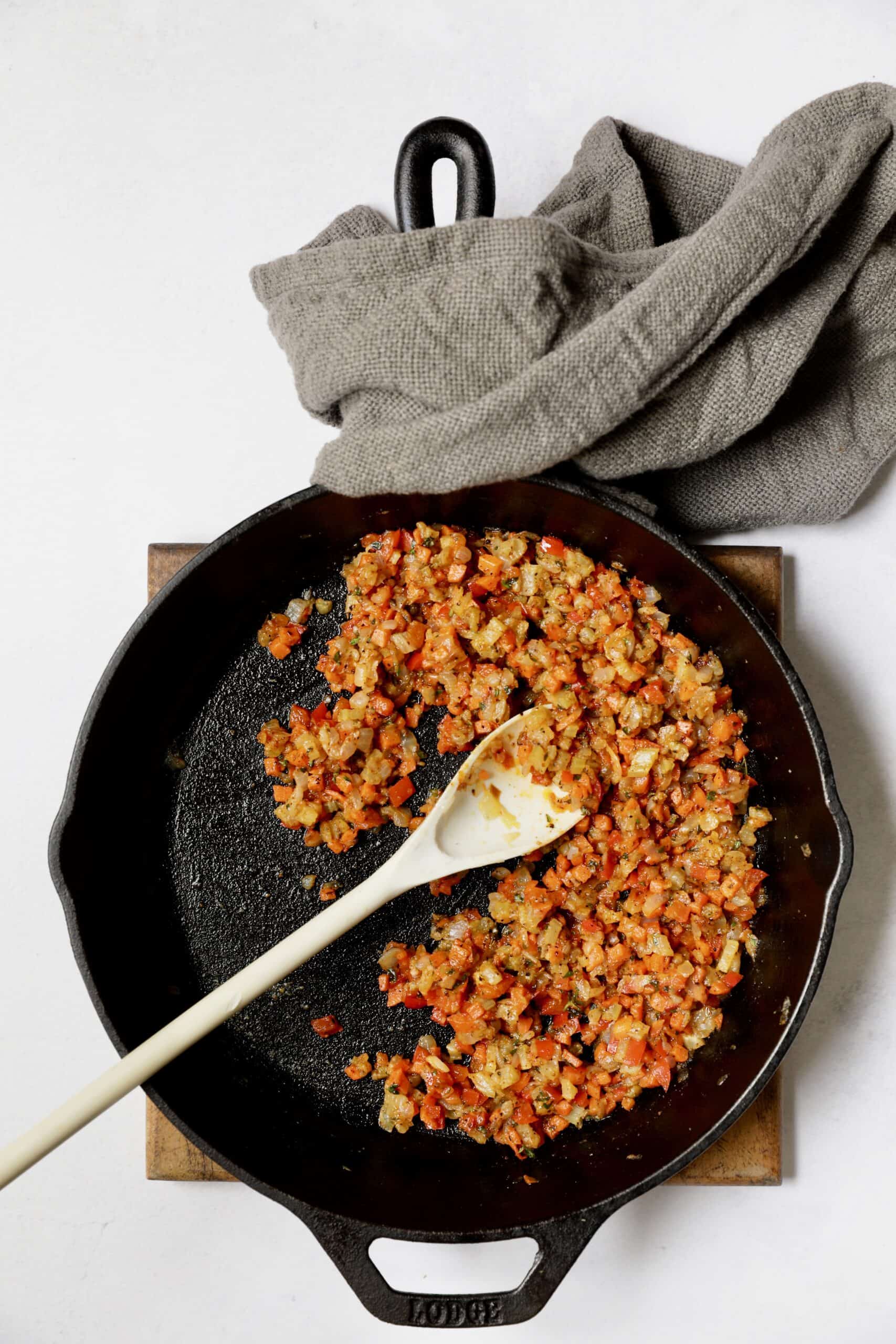 Photo of cooked vegetables in cast iron skillet being stirred with white spoon.