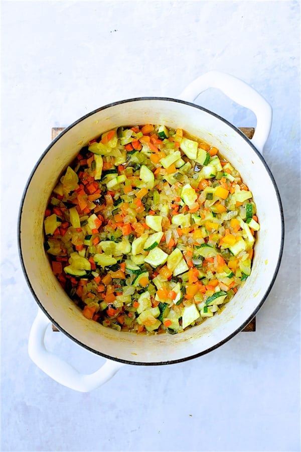 Photo of chopped vegetables being cooked in white Dutch oven.