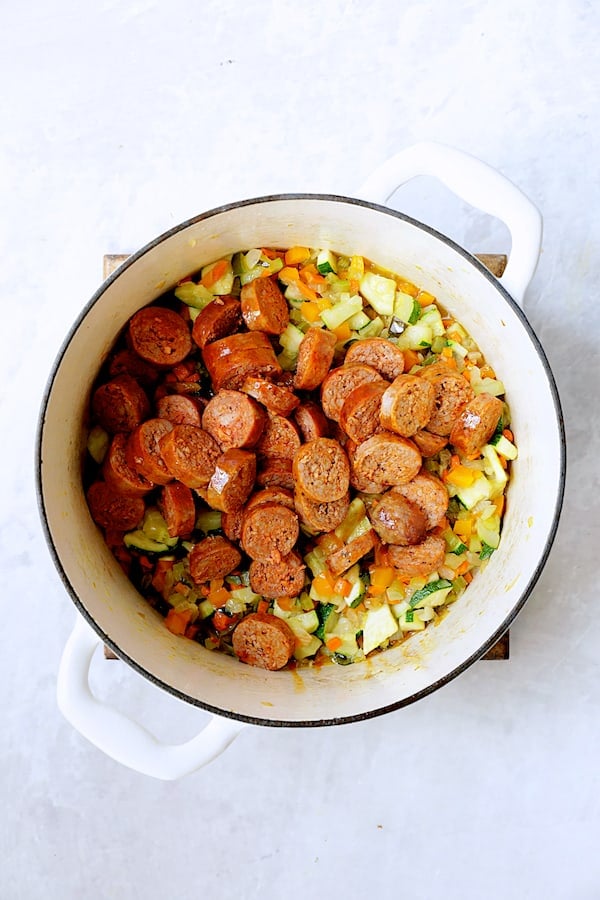Photo of vegetables and sliced chorizo in white Dutch oven.