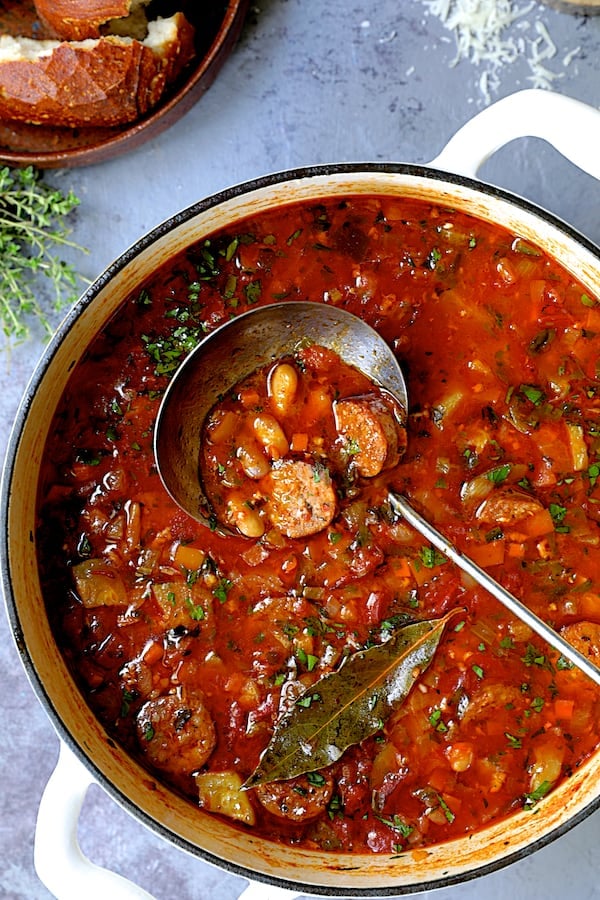 Photo of Chorizo White Bean and Vegetable Soup in white Dutch oven with soup ladle.