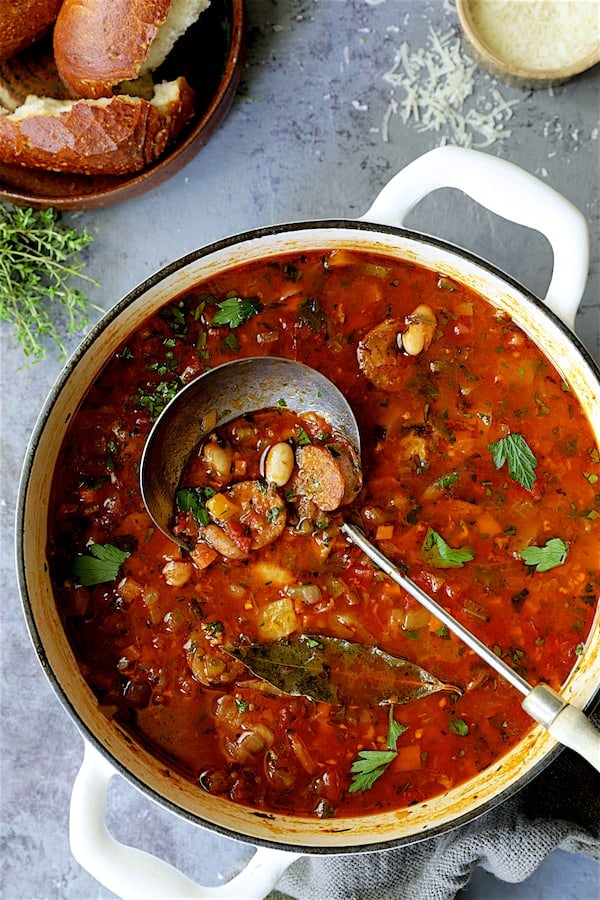 Photo of Chorizo White Bean and Vegetable Soup in white Dutch oven with soup ladle.